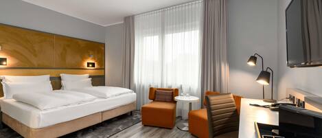 Habitación de hotel con cama, escritorio con silla, una mesita y televisor.