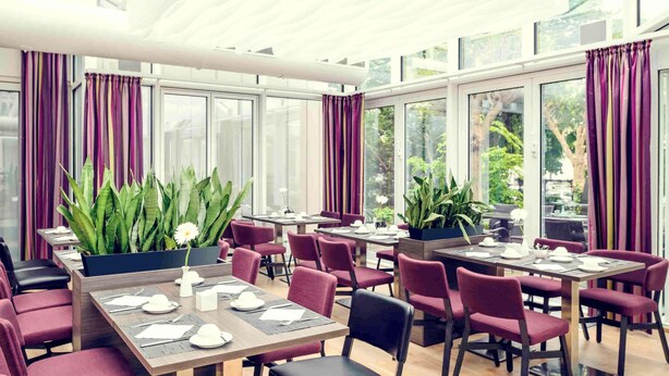 Un comedor moderno con mesas dispuestas para cuatro personas, ventanas amplias y plantas en macetas.