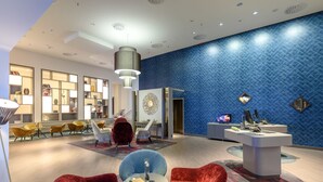 Un vestíbulo moderno con pared de diseño azul, un mostrador de recepción y zonas de estar con sillas rojas y azules.