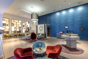 Un vestíbulo moderno con pared de diseño azul, un mostrador de recepción y zonas de estar con sillas rojas y azules.