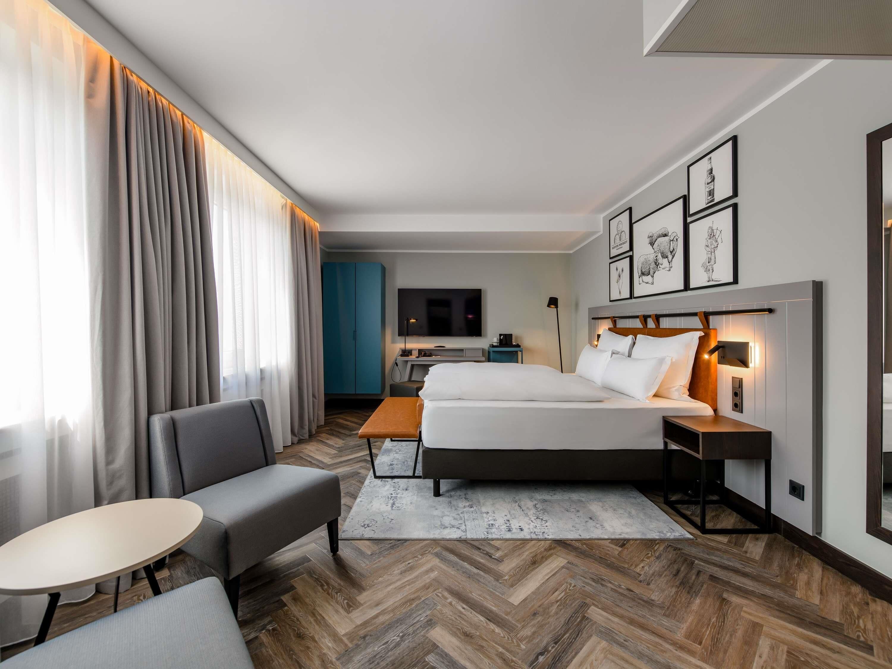 Una habitación de hotel moderna con cama, sofá, una mesita, escritorio y televisión.
