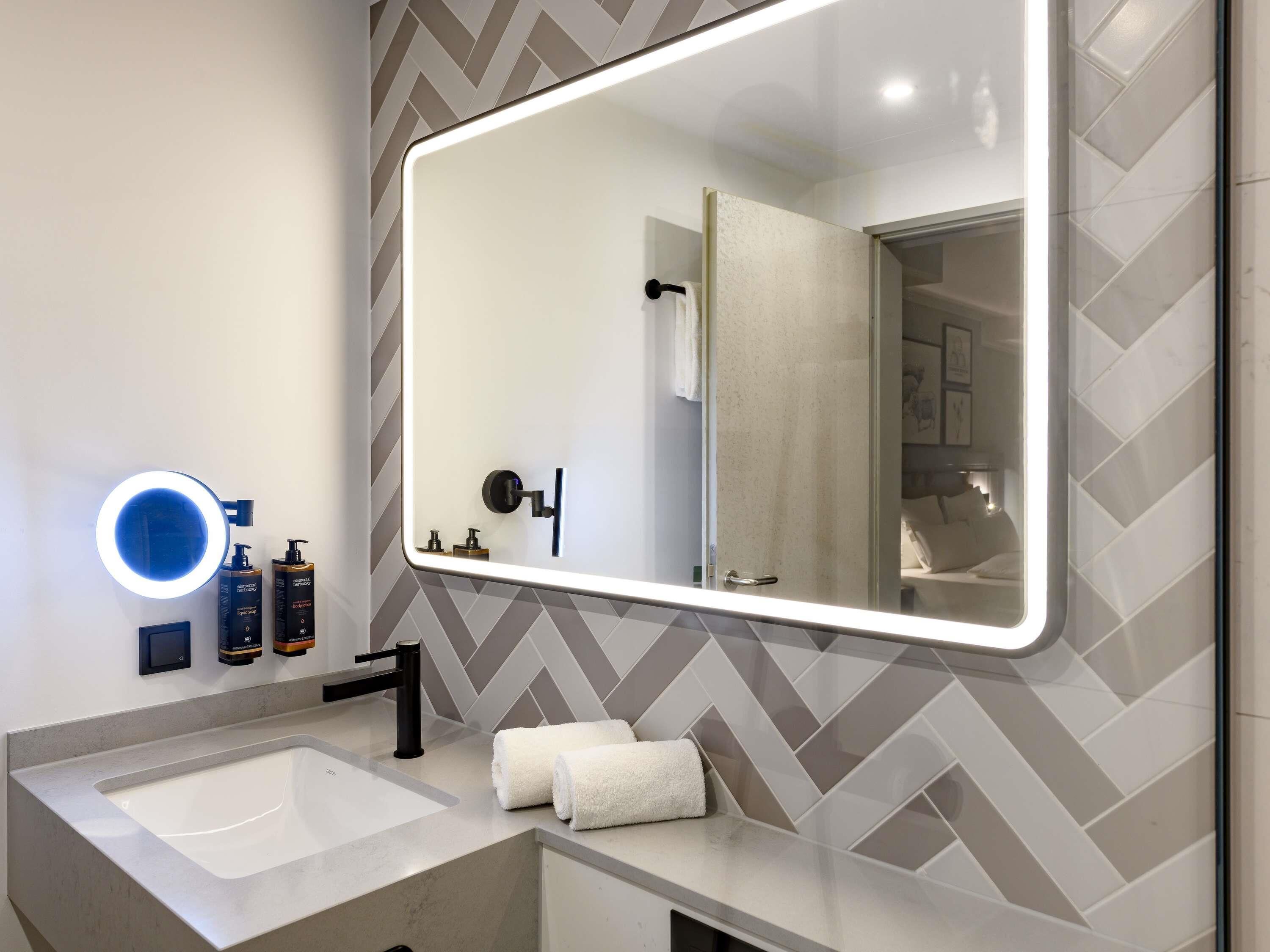 Un baño moderno con un espejo grande, un tocador redondo y una ducha que se ve en el reflejo.
