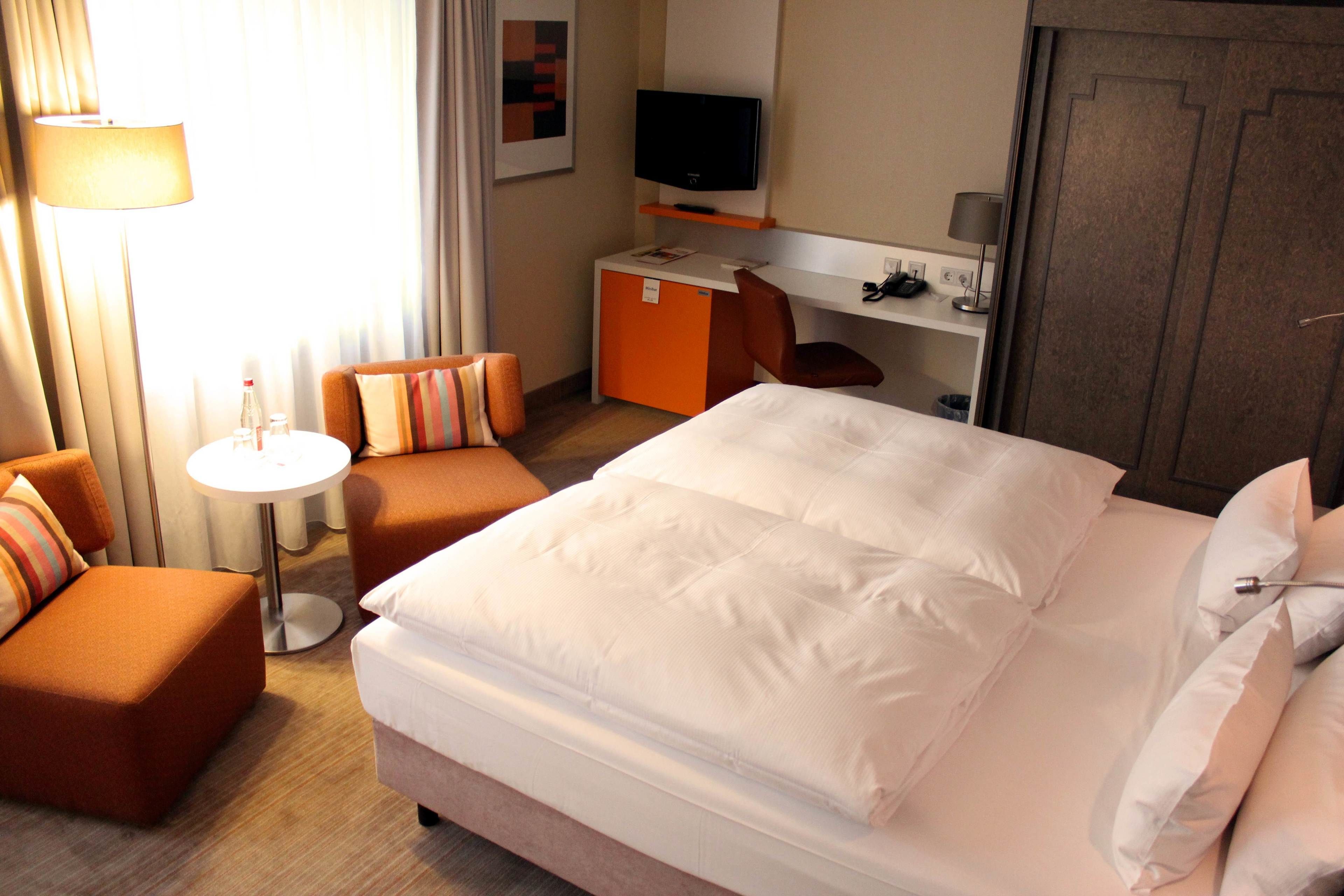 A hotel room with a large bed, a desk, a television, and a seating area with a lamp.