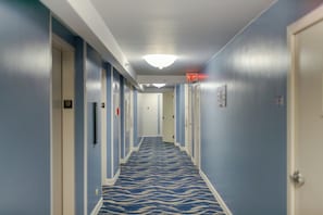 A hotel hallway with a patterned carpet, doors, and an exit sign.