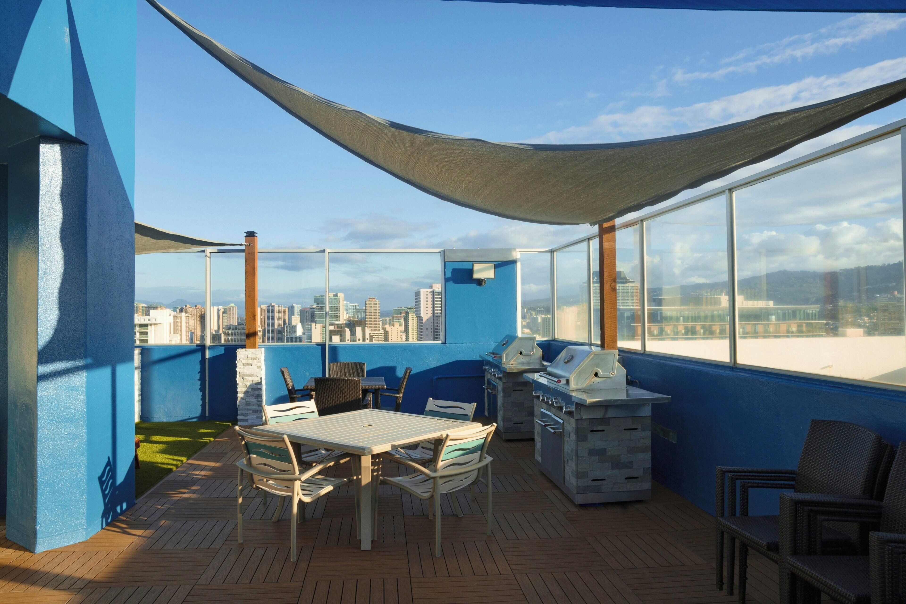 Terraço no telhado com vista para a cidade, uma mesa com cadeiras e churrasqueiras.