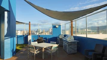 Terraço no telhado com vista para a cidade, uma mesa com cadeiras e churrasqueiras.
