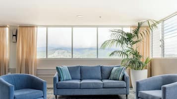 A modern living room with a sofa, two armchairs, a large window with a view, and a potted plant.