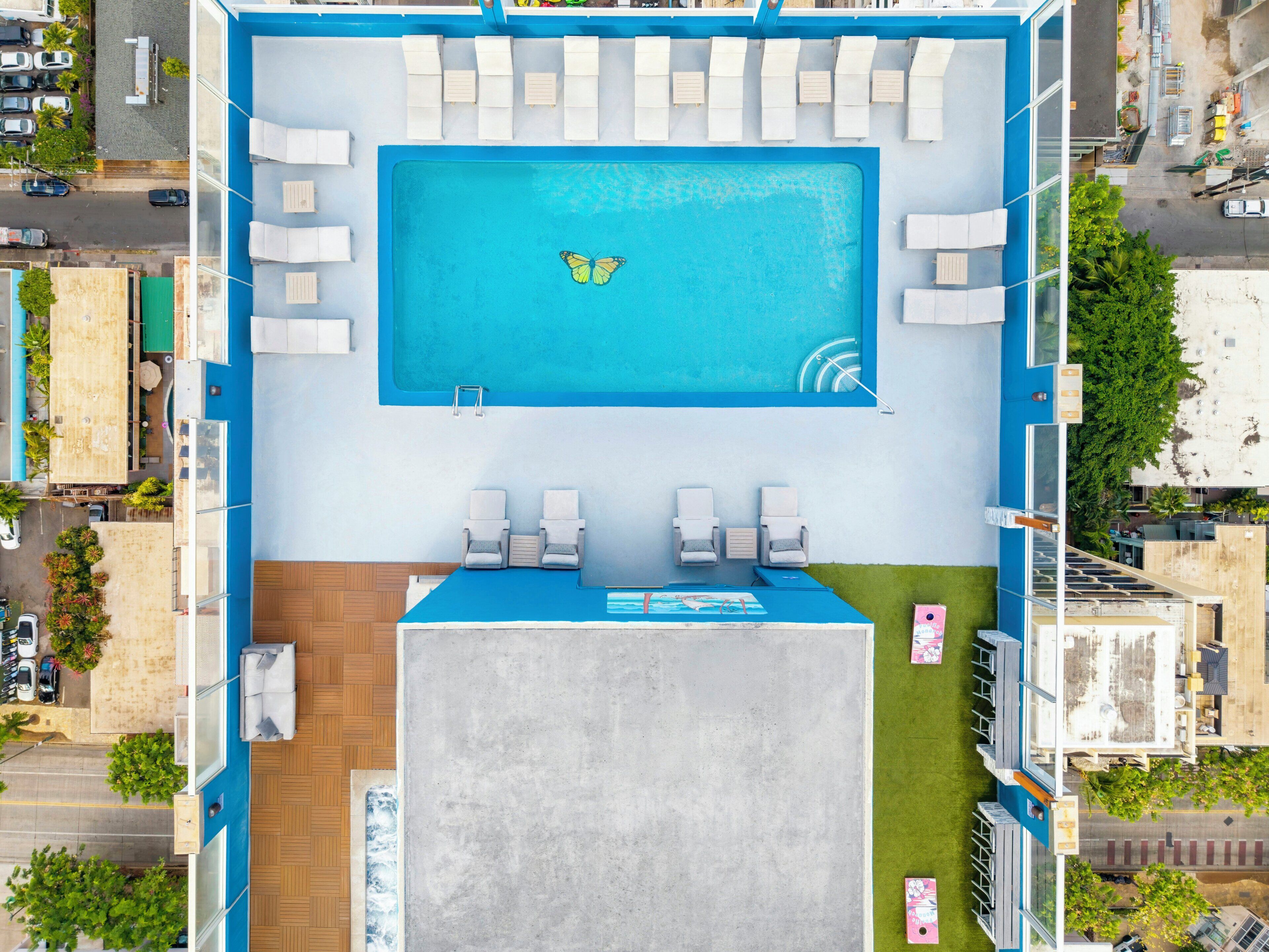 Vue aérienne d’un hôtel avec une piscine, des chaises longues et un petit espace aménagé en terrasse.
