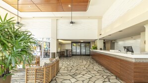 A reception area with a stone-patterned floor, wooden reception desk, and a seating area with a woven bench. - Pacific Monarch Hotel (Honolulu)