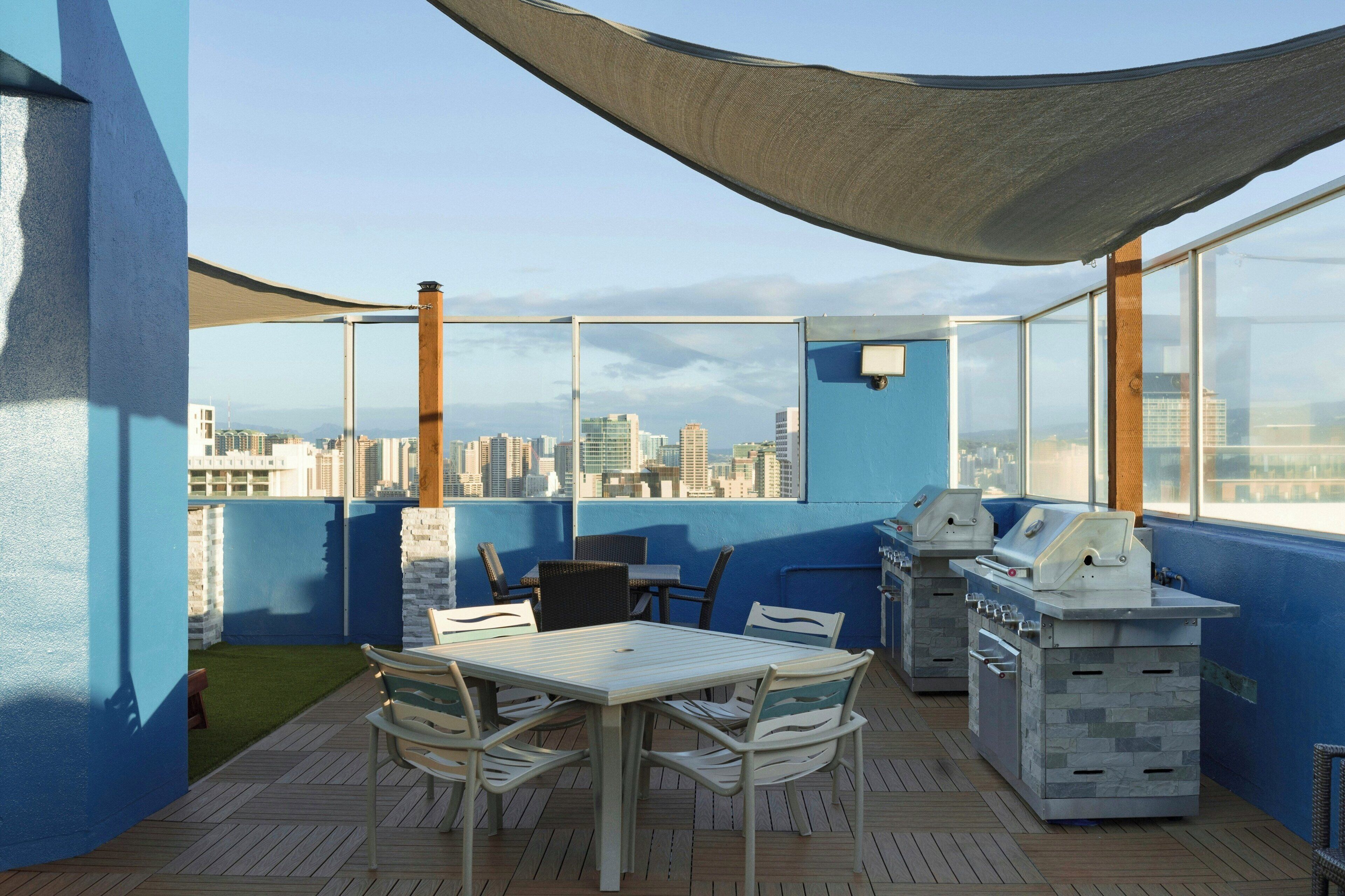 Una terraza en la azotea con mesa y sillas, una parrilla y vistas al horizonte de la ciudad.