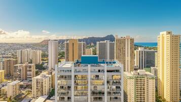 Um edifício alto com várias varandas, piscina no terraço e vista para a cidade e montanhas ao fundo.