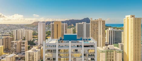 Un edificio moderno con varios balcones, una piscina en la azotea y vistas a la ciudad y montañas al fondo.