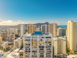 Un edificio moderno con varios balcones, una piscina en la azotea y vistas a la ciudad y montañas al fondo.