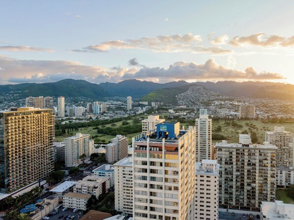 A high-rise building with multiple floors, surrounded by other high-rise buildings, and a mountainous landscape in the background.