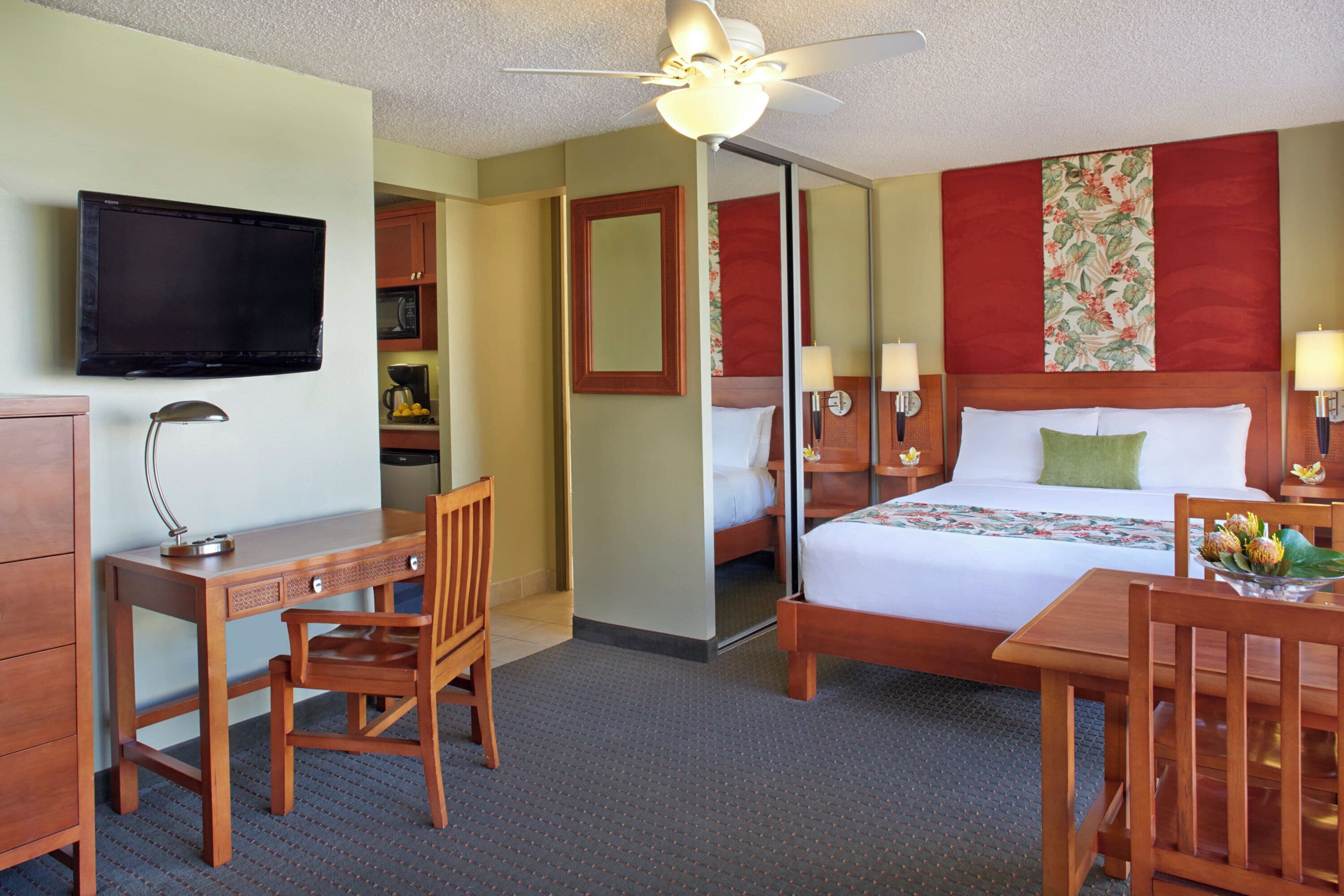 A hotel room with a bed, desk, chair, television, and a ceiling fan.