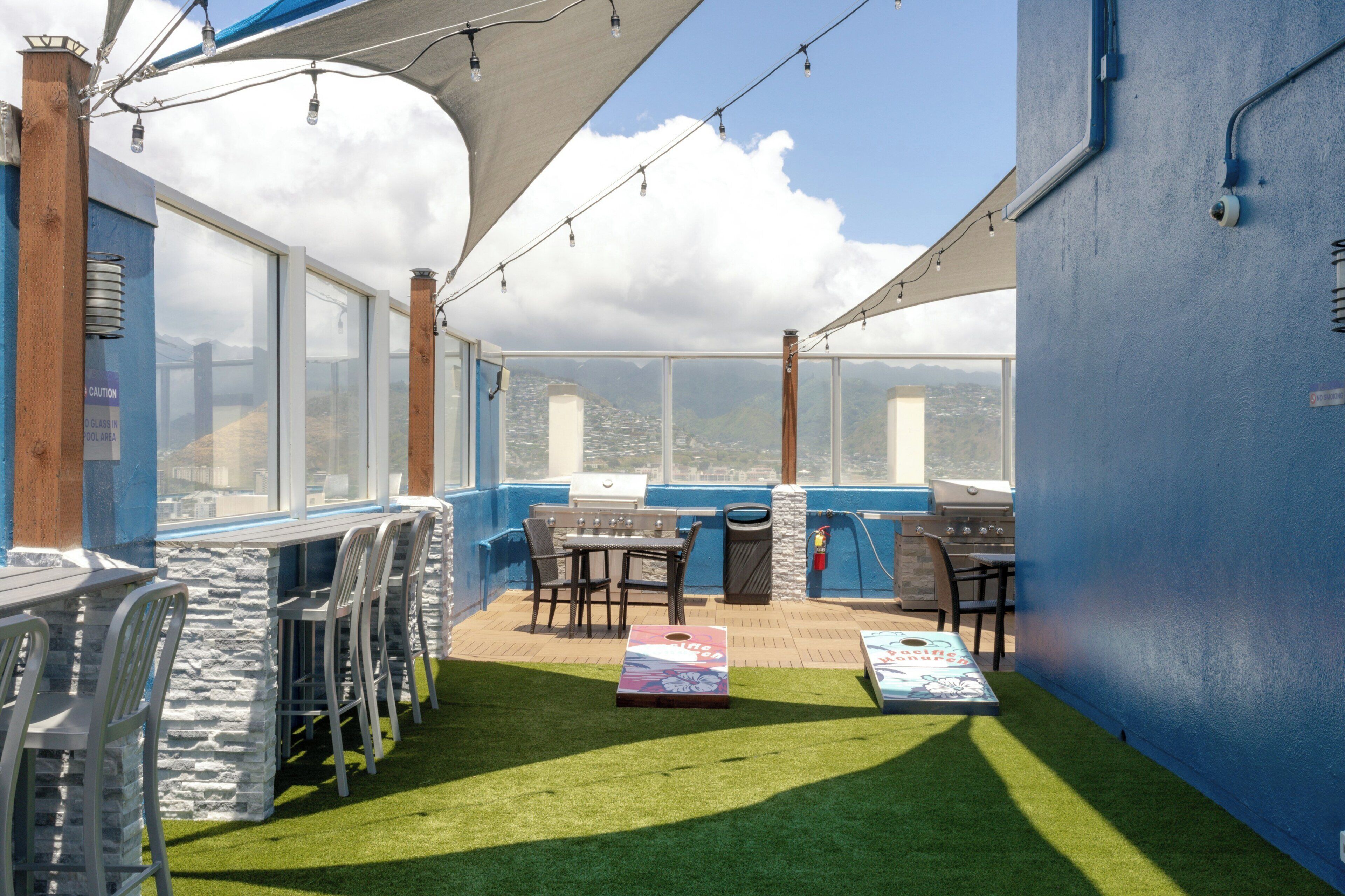 A rooftop patio with a grill, seating, and a view of the cityscape.