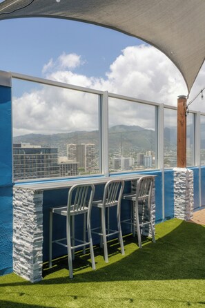 A balcony with two chairs, a table, and a view of a cityscape and mountains. - Pacific Monarch Hotel (Honolulu)
