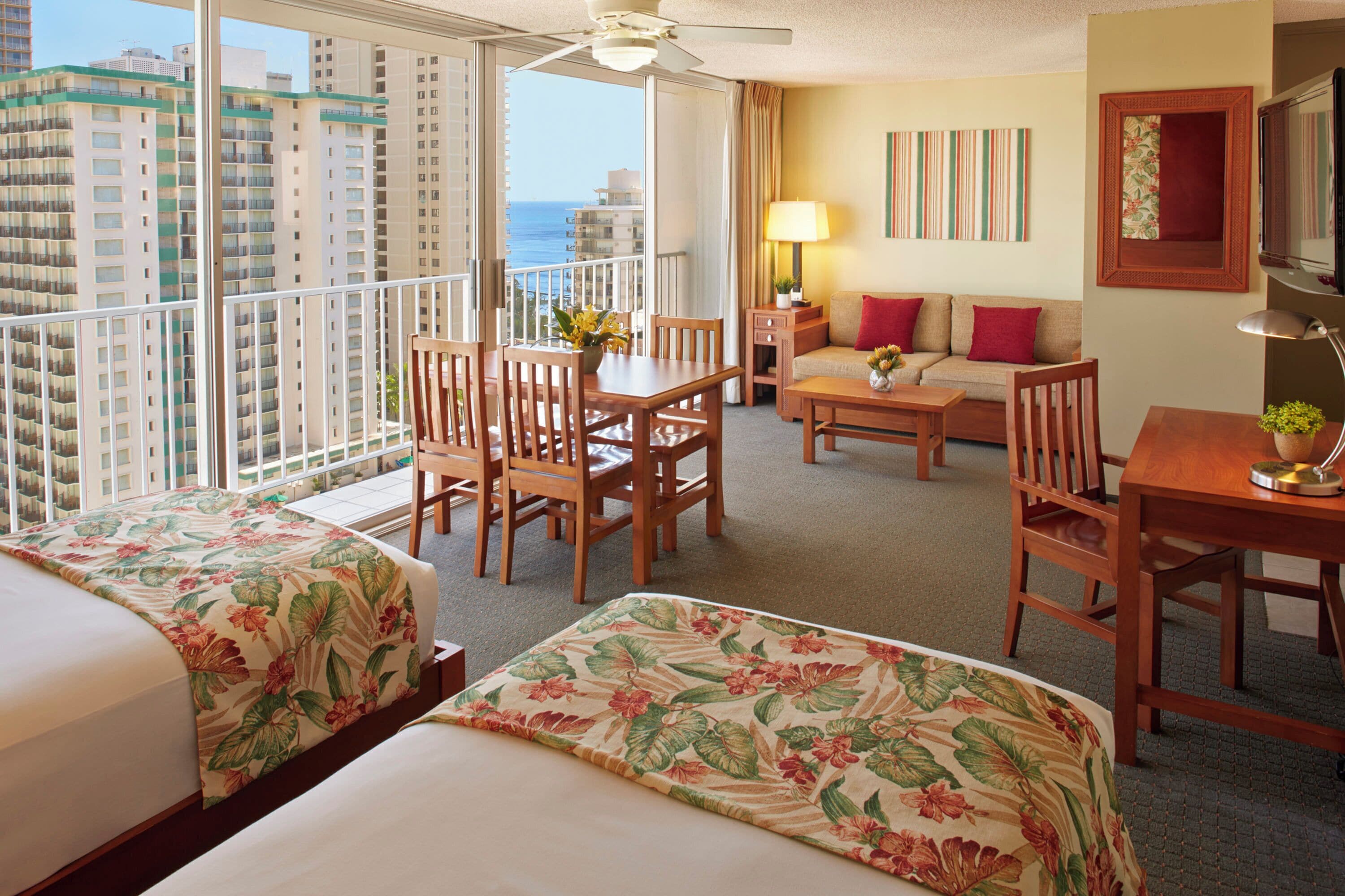 Quarto de hotel com duas camas, varanda, área de refeições e um sofá.