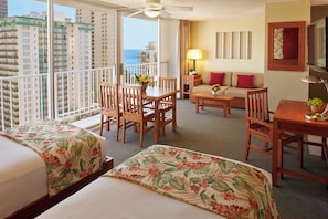 Habitación de hotel con dos camas, un balcón, zona de comedor y un sofá.