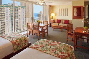 A hotel room with two beds, a balcony, a dining area, and a sofa.