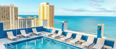A rooftop pool with lounge chairs and a view of the ocean.