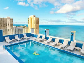 A rooftop pool with lounge chairs and a view of the ocean.
