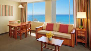 A hotel room with a dining table, sofa, and a view of the ocean.