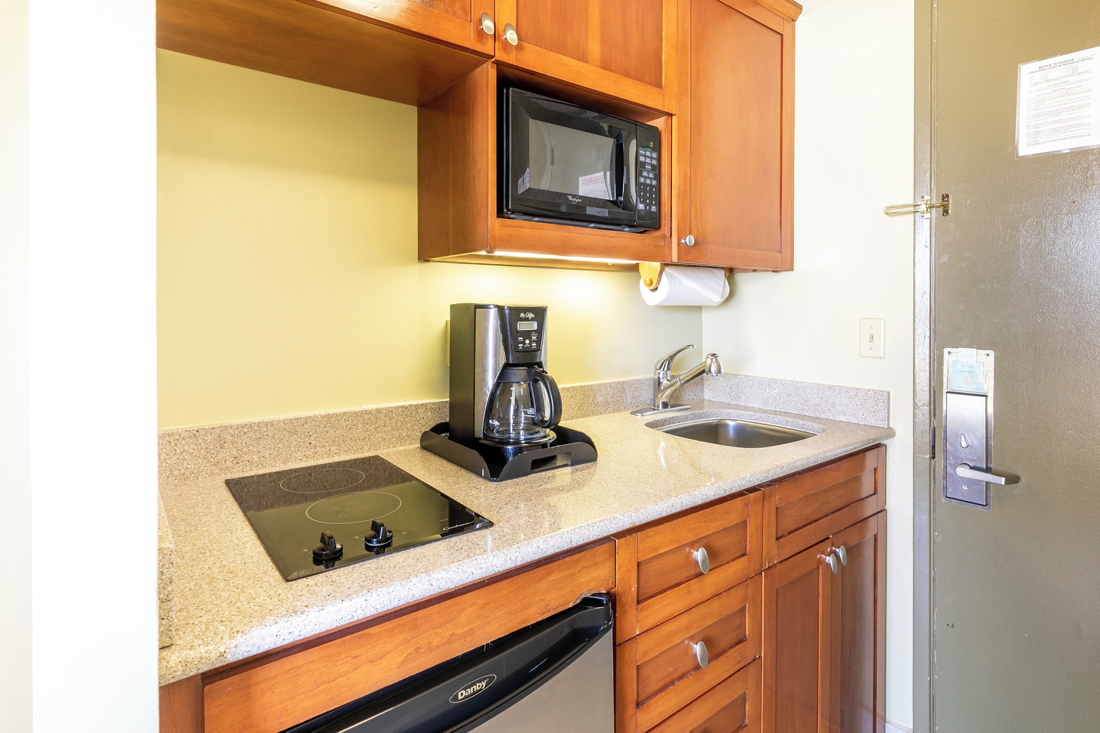 Una cocina compacta equipada con microondas, cafetera, lavabo y lavavajillas.