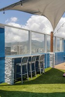 Un bar en la azotea con vista a un paisaje urbano, que incluye edificios y montañas.