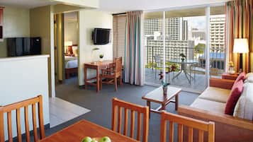 Habitación de hotel con comedor, sofá, televisor y balcón con vista a la ciudad.