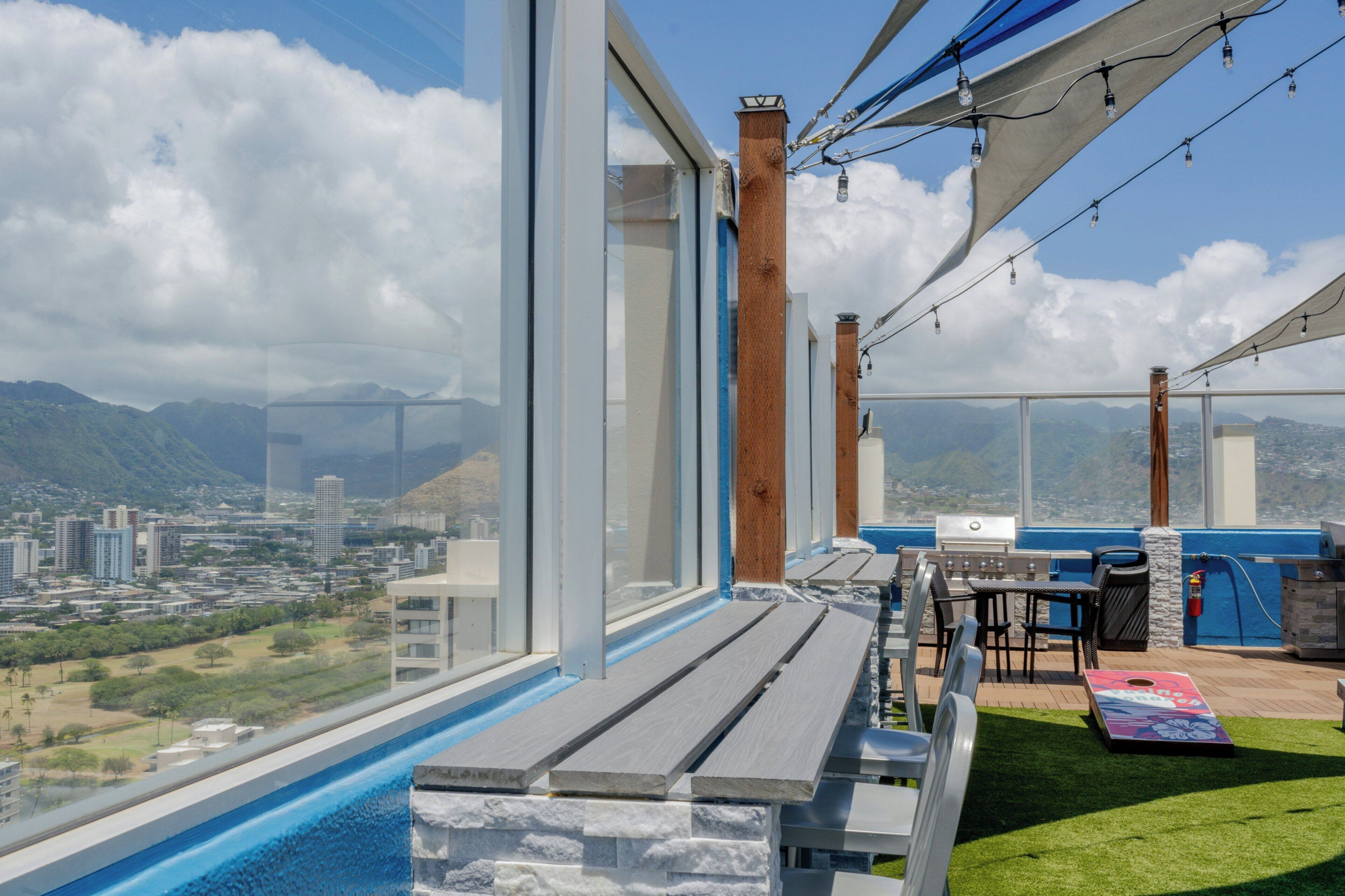 A modern outdoor terrace with a pool, dining area, and a view of a cityscape and mountains.
