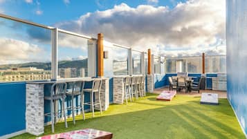 A rooftop terrace with a bar area, outdoor seating, and a view of the cityscape.