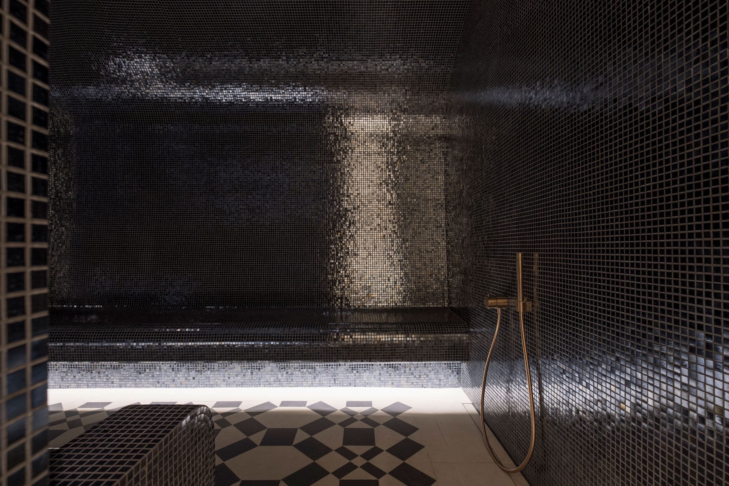 Un baño con piso de baldosas, zona de ducha y pared con diseño de cuadrícula.