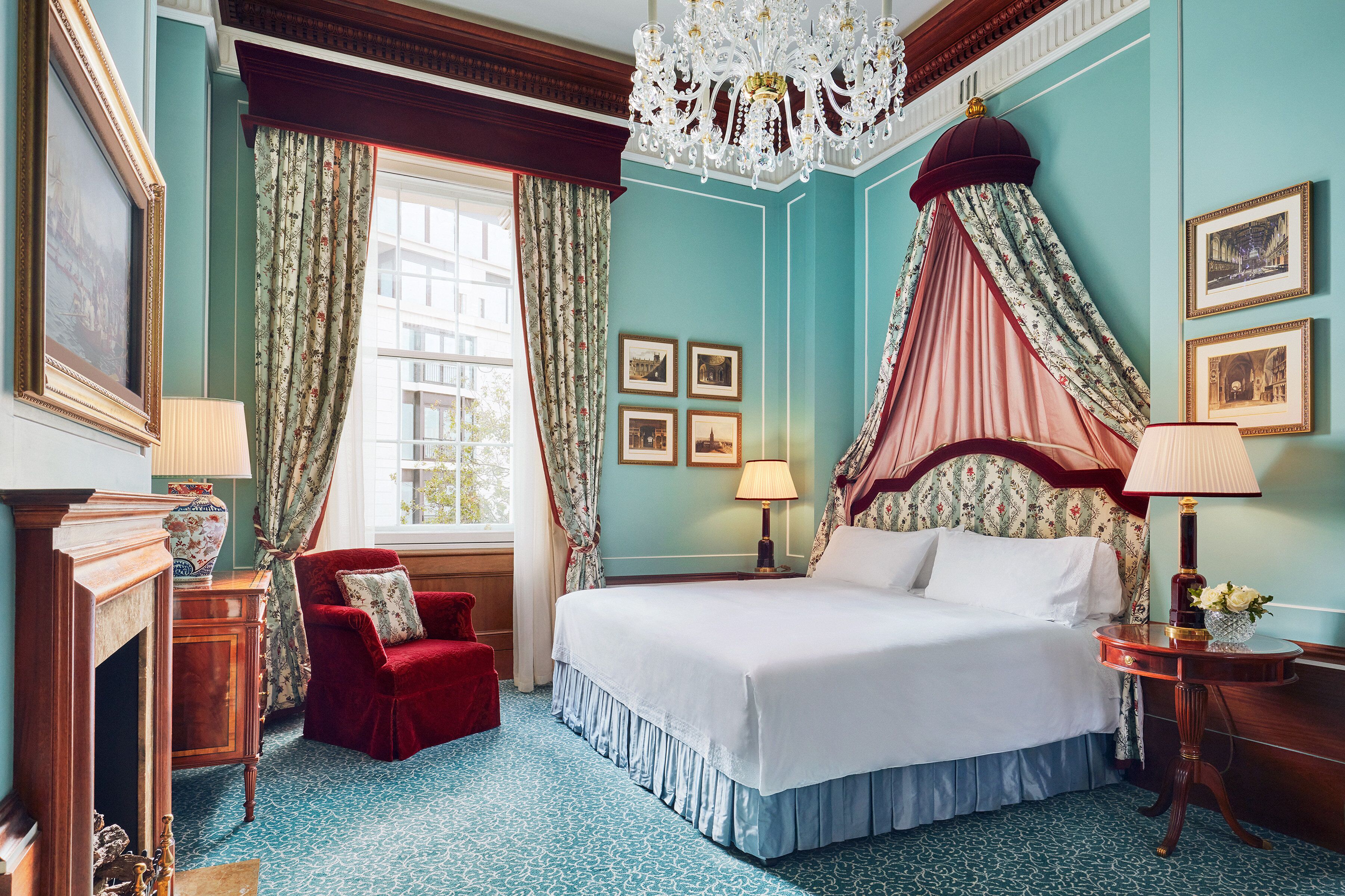 A bedroom with a four-poster bed, a red armchair, a chandelier, and framed pictures on the wall.