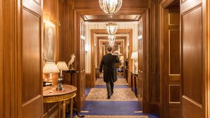 A hallway with wooden paneling, a blue carpet, and a chandelier. - The Lanesborough, Oetker Hotels (London)