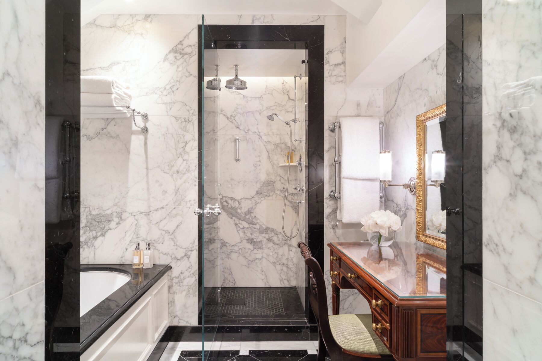 A modern bathroom with a glass-enclosed shower, marble walls, a vanity with a mirror, and a bathtub.