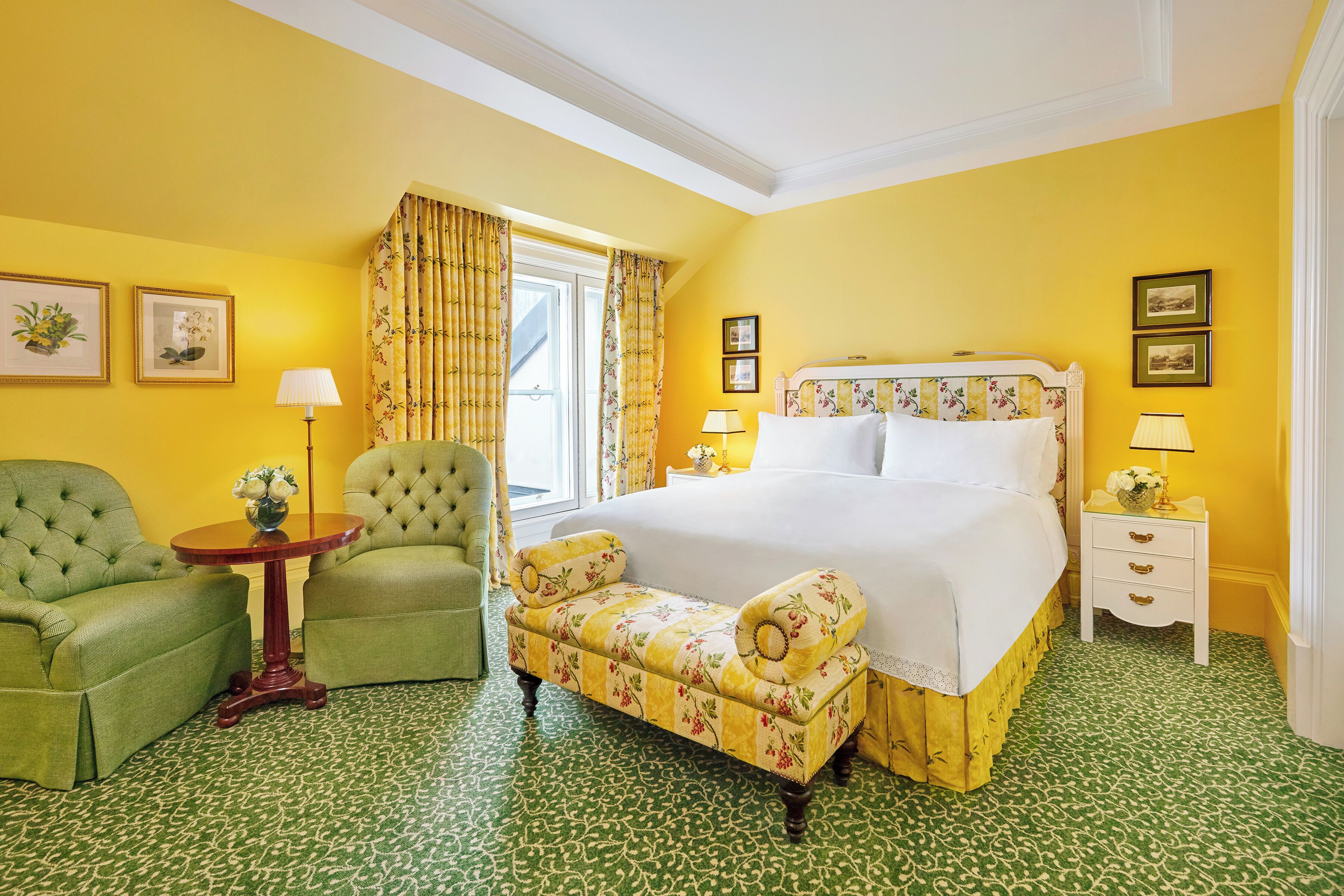 A hotel room with a large bed, two armchairs, a small table, and a nightstand with lamps.