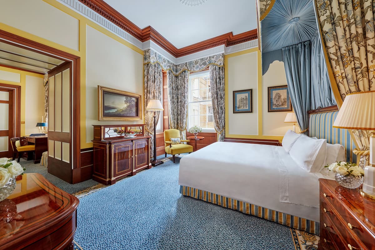 A hotel room with a large bed, a desk, a chair, a television, and a window with curtains.