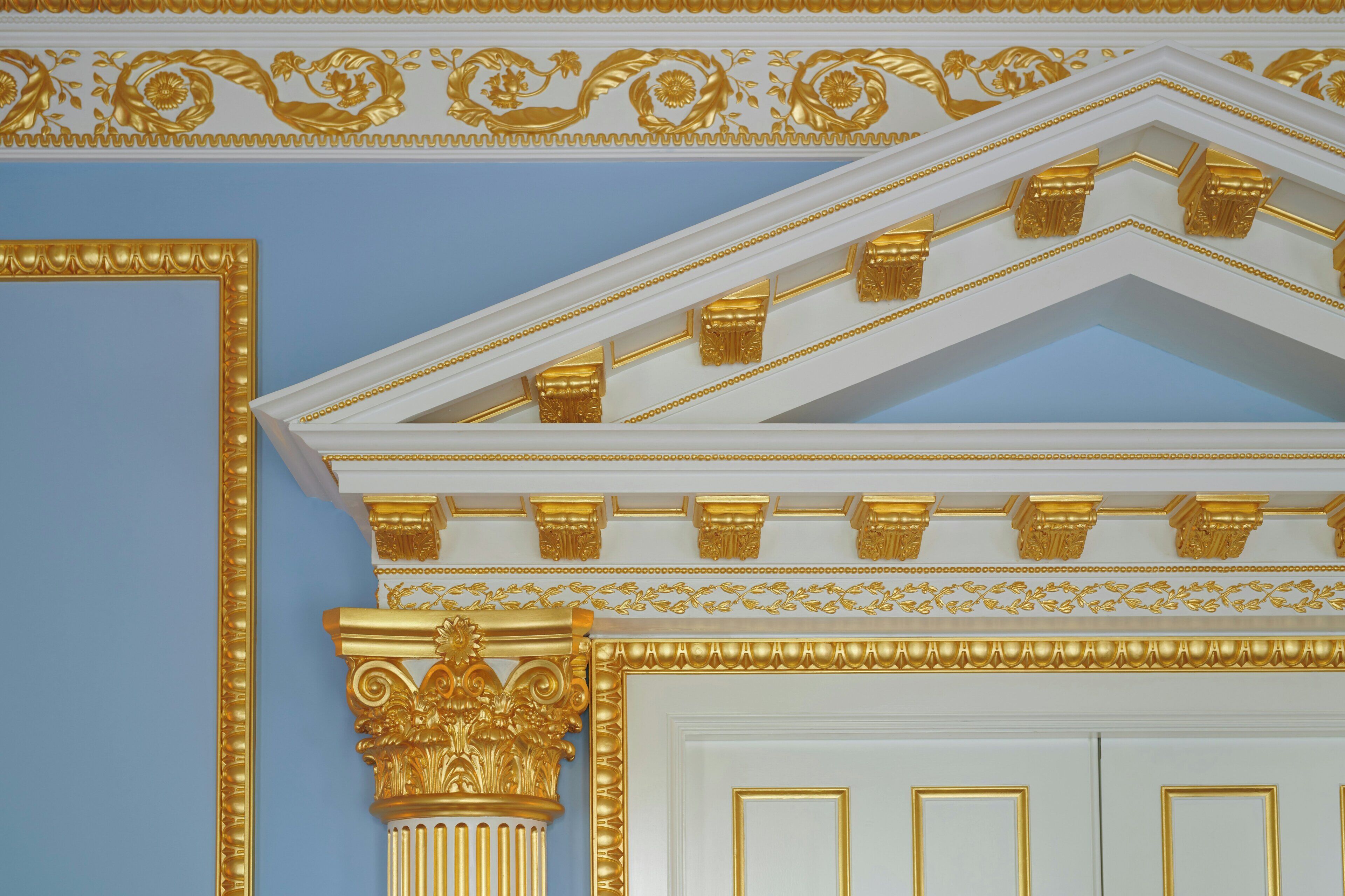 A room with a white door, gold decorative moldings, and a blue wall.