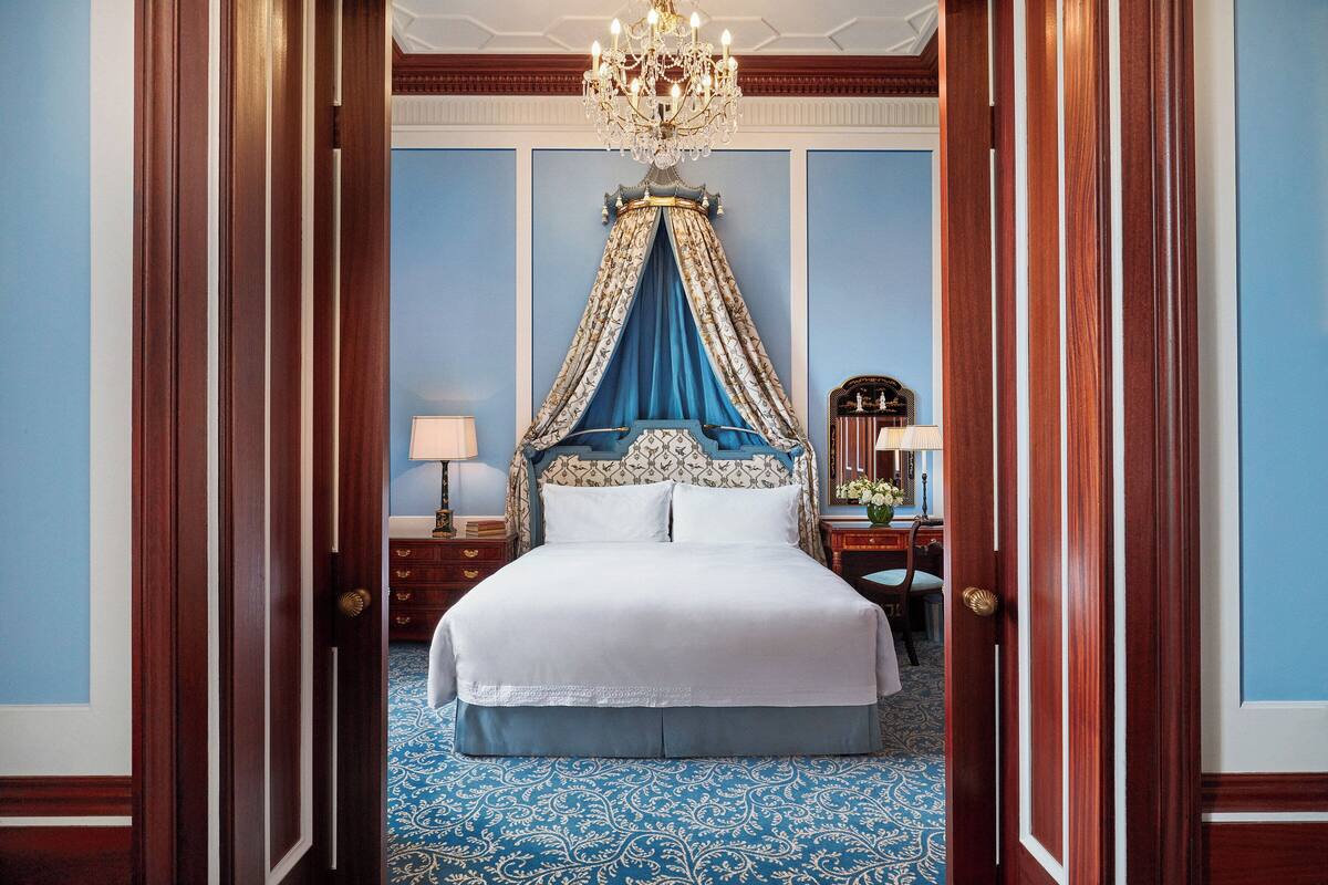 Una cama grande y ornamentada con dosel, una araña y una alfombra azul estampada.