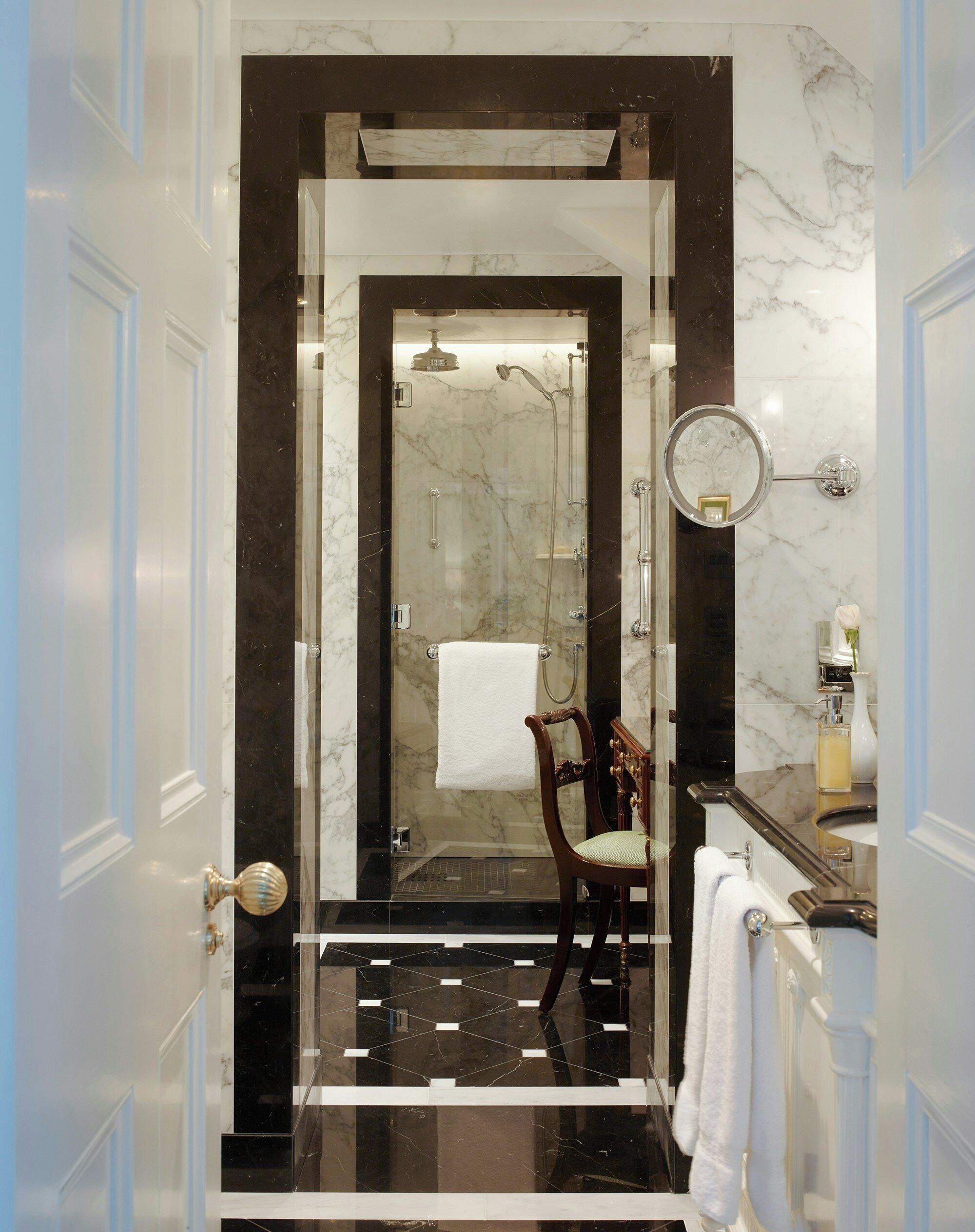 A bathroom with a shower, a chair, a mirror, and a sink.