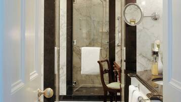 A bathroom with a shower, a chair, a mirror, and a sink.