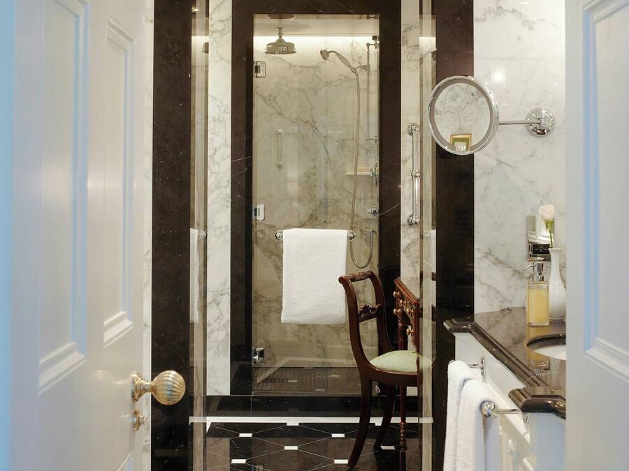 A bathroom with a shower, a chair, a mirror, and a sink.