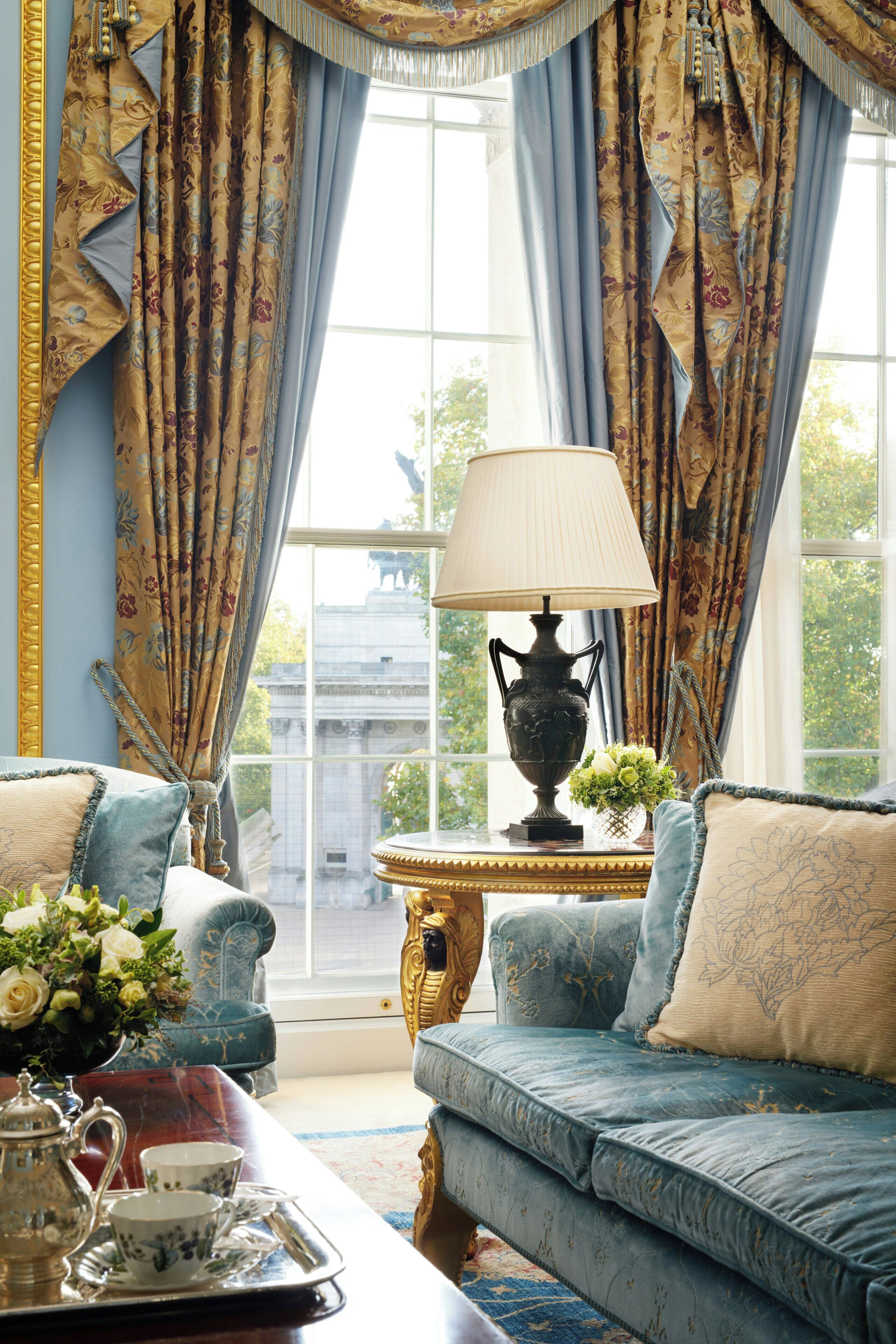 A room with a blue sofa, a table with a lamp, and curtains.