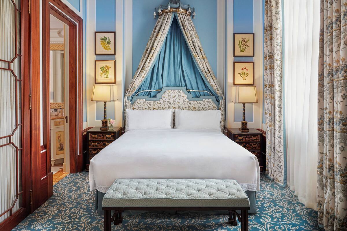 Un dormitorio con una cama con dosel, un banco al pie de la cama y una alfombra estampada.
