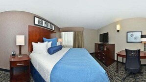 Habitación de hotel con una cama grande, un escritorio, una silla, un televisor y un cuadro en la pared.