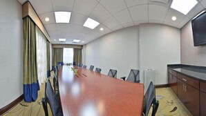 Un salón de conferencias con una larga mesa, sillas, una pantalla de proyector y un gran ventanal con cortinas.