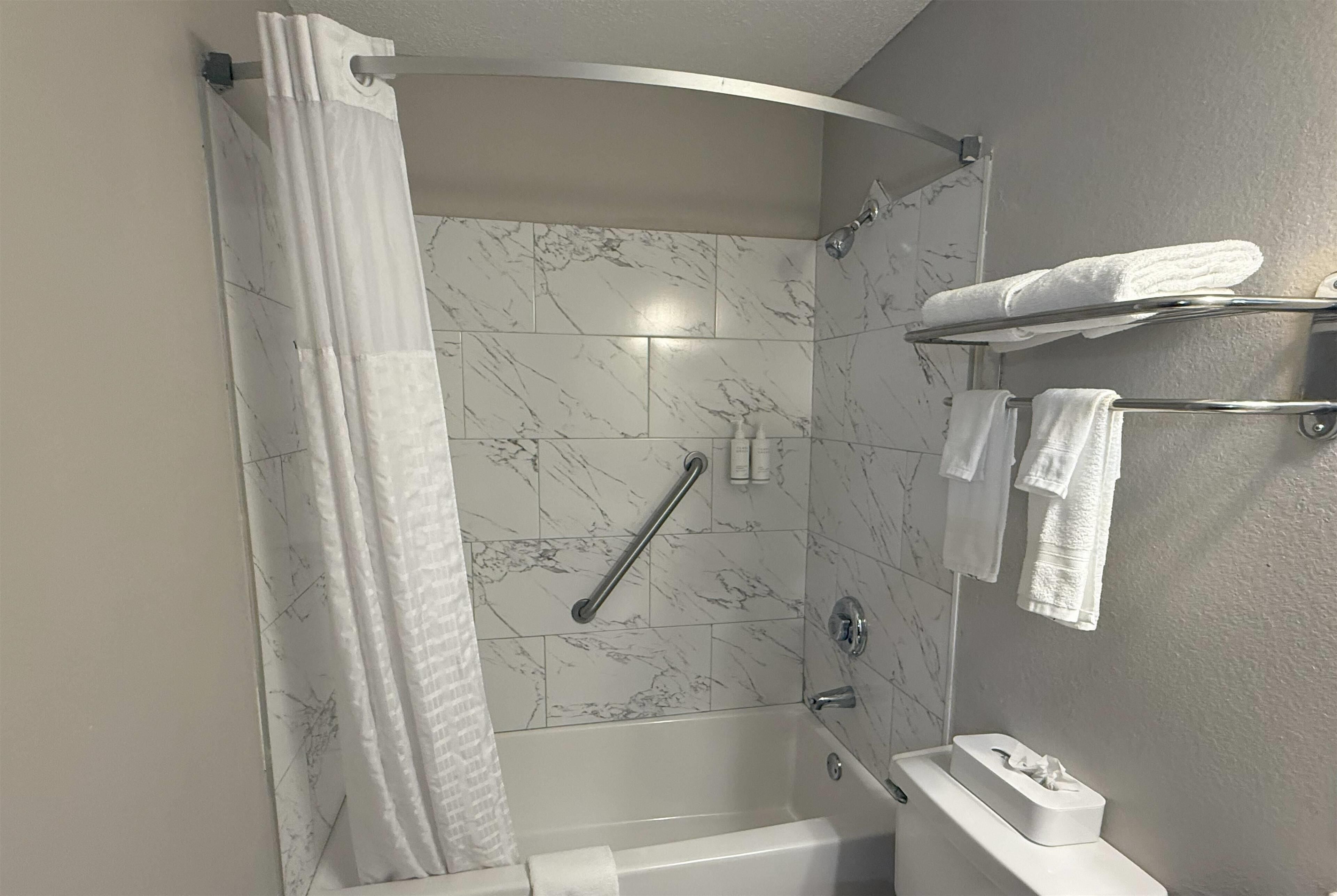 Une salle de bain avec une douche, une baignoire et des toilettes. Des serviettes blanches sont suspendues sur un porte-serviettes et une serviette est posée sur le sol.
