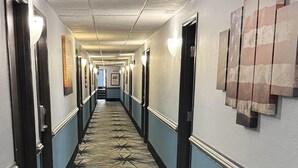 A hotel hallway with a patterned floor, doors, and wall-mounted artwork. - Days Inn by Wyndham Orange Park/Jacksonville (Orange Park)