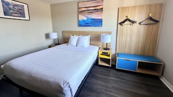 Une chambre d’hôtel comprenant un lit, des tables de chevet, un banc et un mur orné d’un tableau et de deux patères.